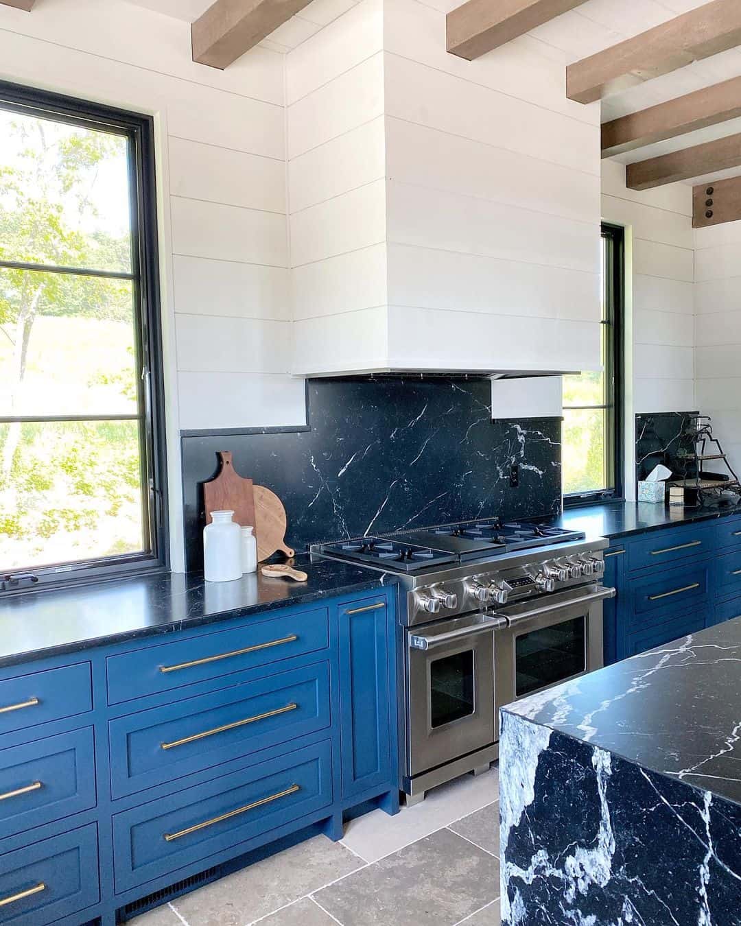 Deep Blue Cabinets With Brass Pulls Frame a Marble Backsplash