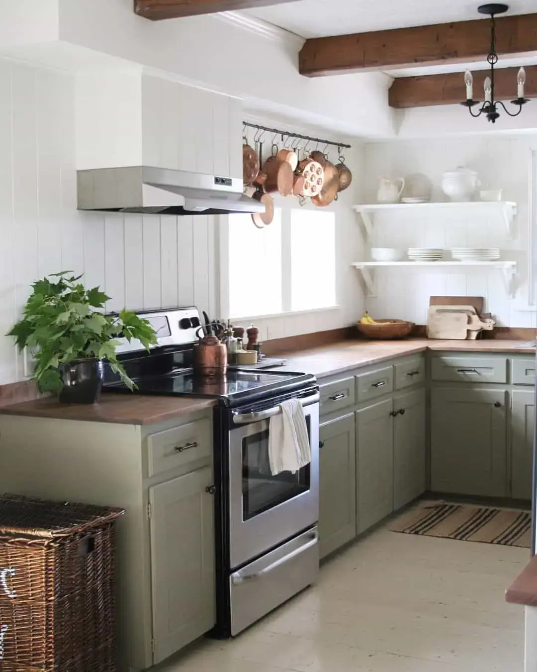Sage green cabinets with a hanging pot rack above the stove
