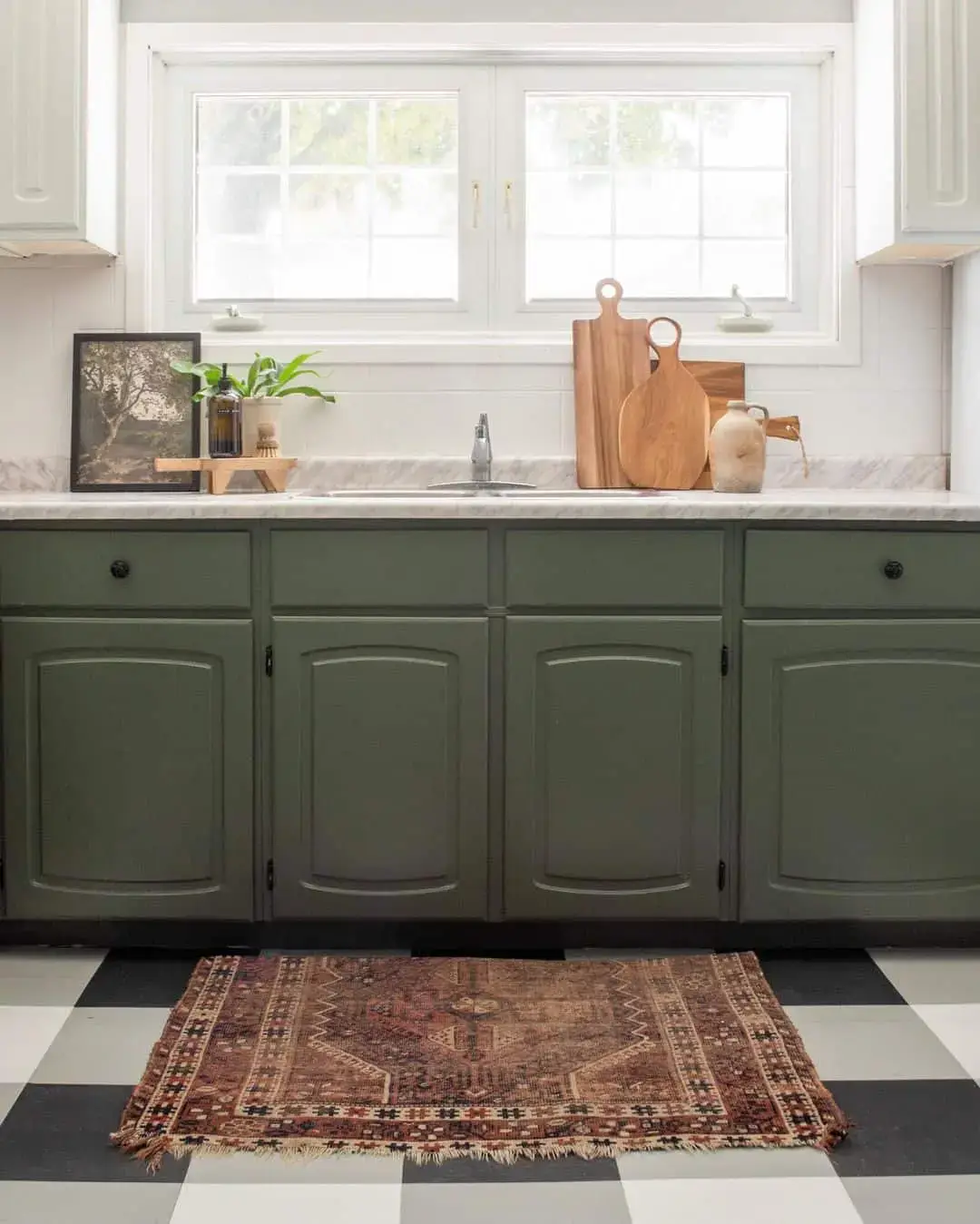 Layer a vintage rug over checkered floors with sage green cabinets