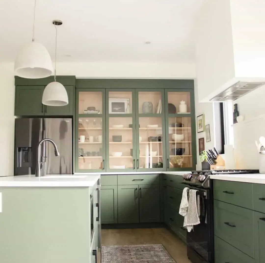 Glass-fronted sage green cabinets display curated dishware