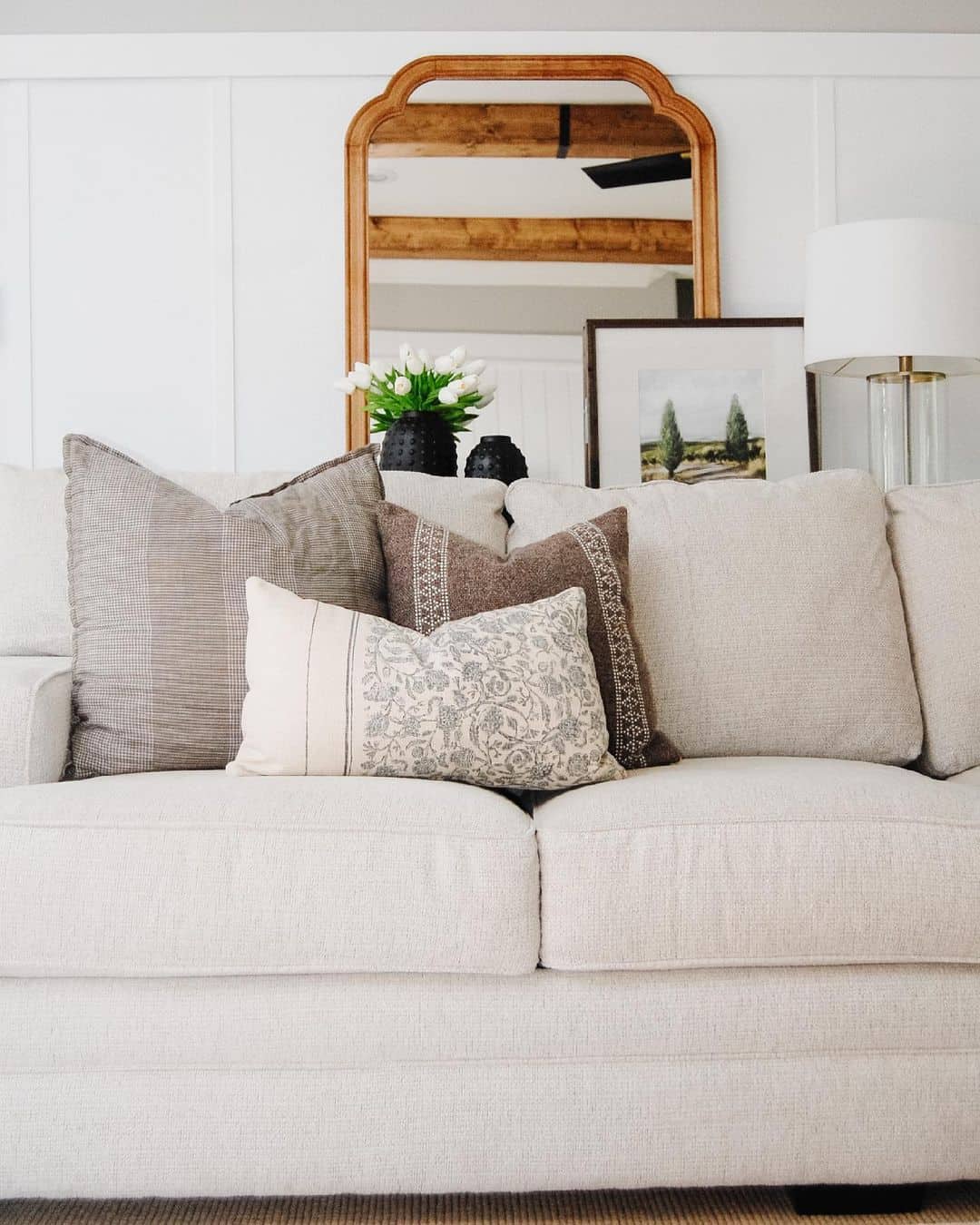 Curved Wood Mirror Frames a Sofa with Textured Pillows